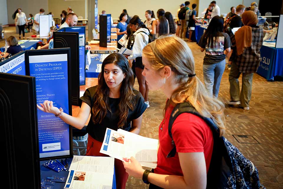 Academic Fair A student speaks with a presenter at a booth during an academic fair. There is a poster that reads "Didactic Program in Dietetics"