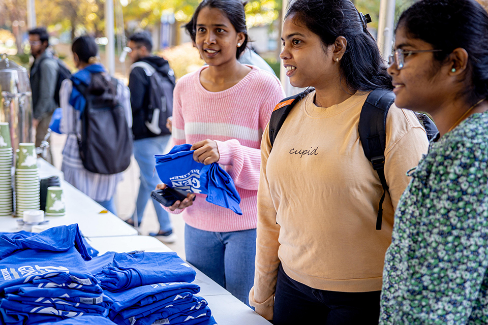 First generation Day Three students talk and select T-shirts from a table.