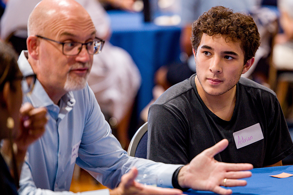 First Generation Families A student and an older male sit at a table during a welcome event.