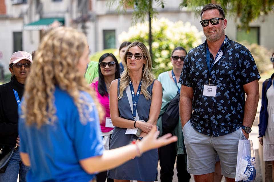 SLU 101 Parents and Families A group of parents stands in a circle as they listen to a female SLU Campus Ambassador speak during a campus tour.