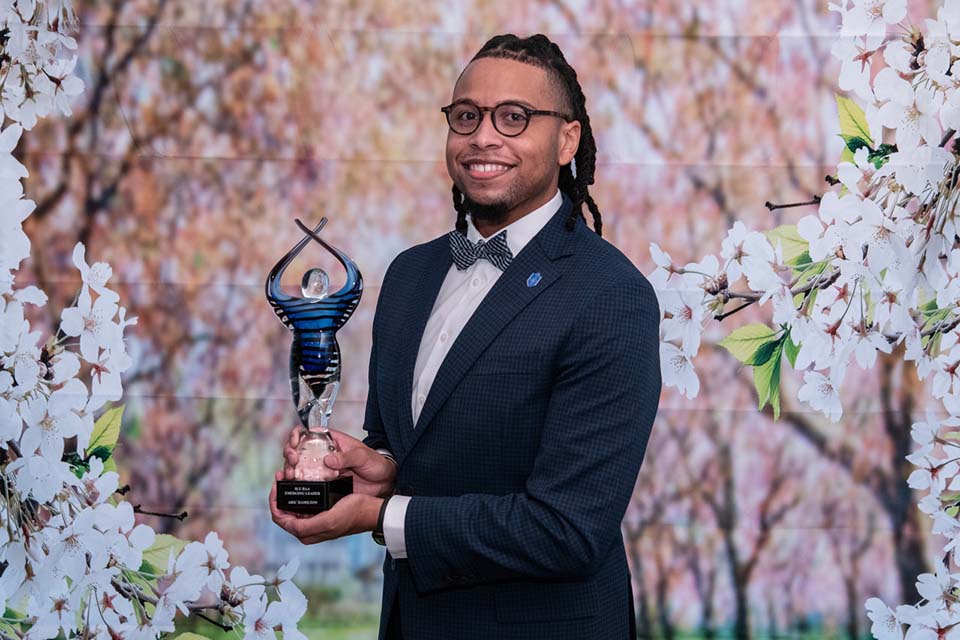 BAA Emerging Leader Award 2025 Aric Hamilton poses for a photo with an award in front of a floral background.