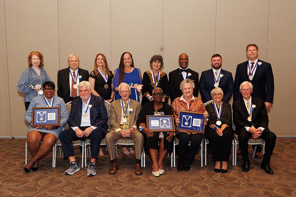 Alumni Merit Awardees 2023 A group of men and women pose for a photo together, some holding framed medals.