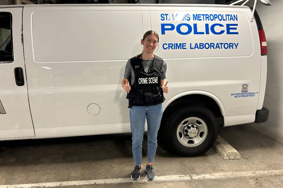 student poses in front of police crime laboratory van