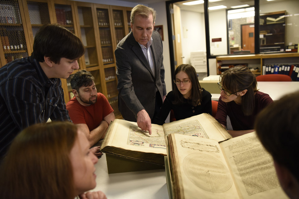 Medieval Studies class Students gathered around a book with a professor