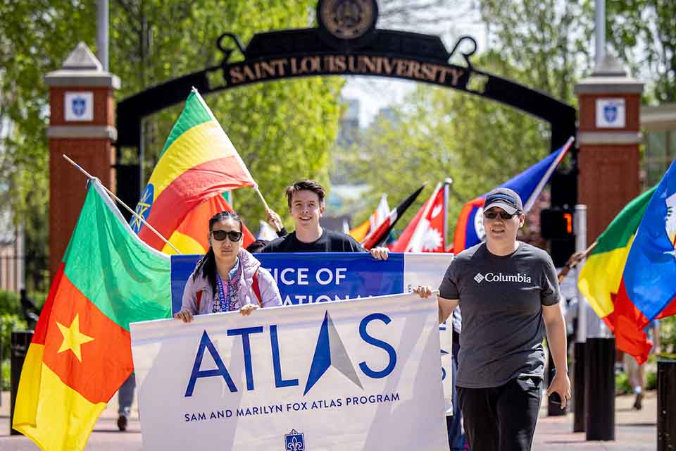 Parade of Nations 2023 Students holding a sign reading Sam and Marilyn Fox Atlas Program in front of a parade of flags