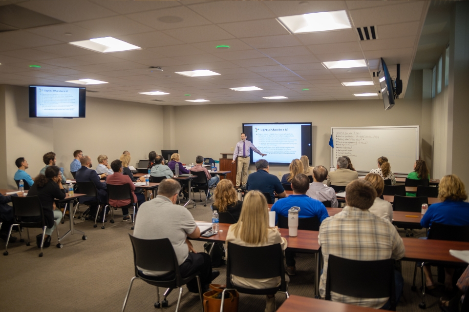 Leadership Development Workshop Participants seated at tables in a classroom setting, with a presenter standing in the front of the room delivering a presentation.
