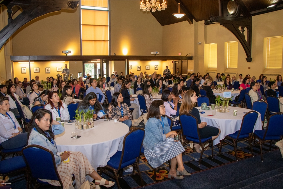 Be Heard 2024 Audience A crowded room of conference attendees are seen from the front while sitting at tables, watching a presentation