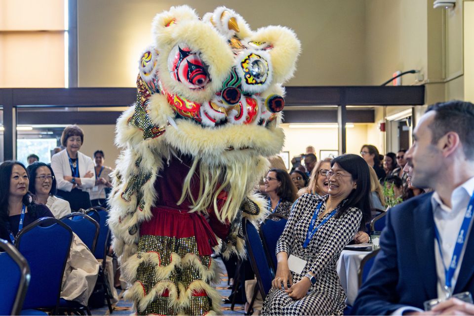 Be Heard Conference Lion Dance Performer Audience members react to a lion dance performer in an elaborate costume with artificial fur and colors that form a lion's face.