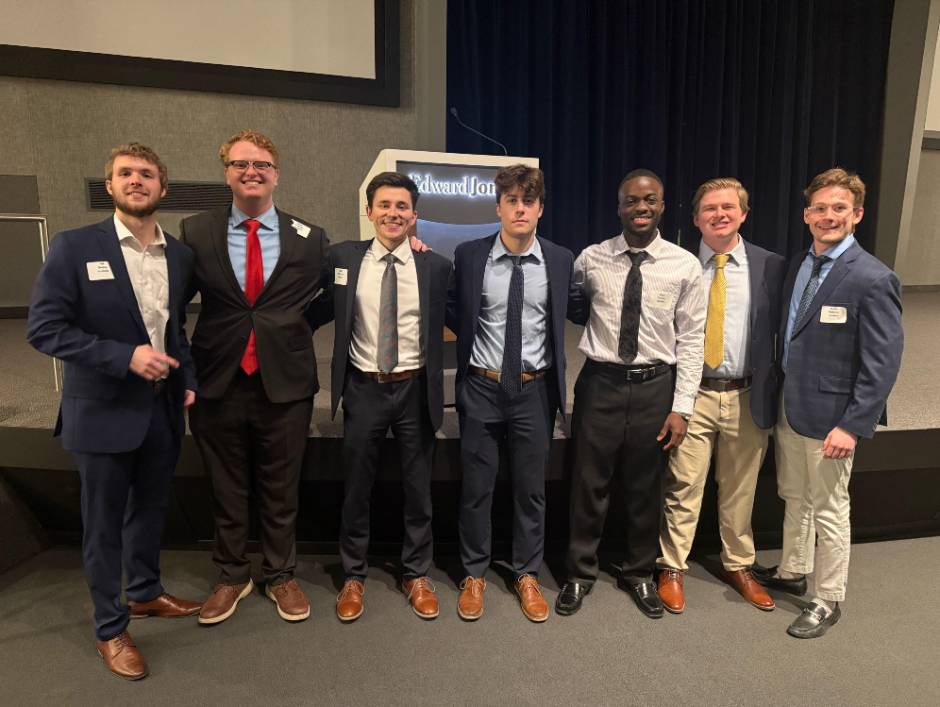 Team members pose in front of a stage while wearing business attire SLU's 2025 CFA team
