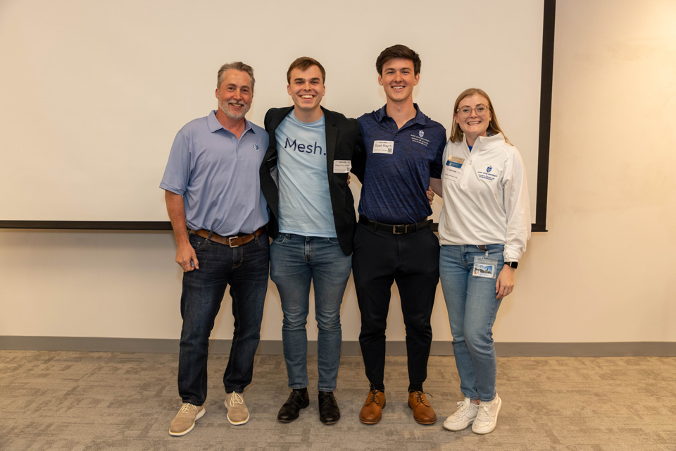 Entrepreneurship Team Four students, faculty and staff stand at the front of a classroom in front of a whiteboard.