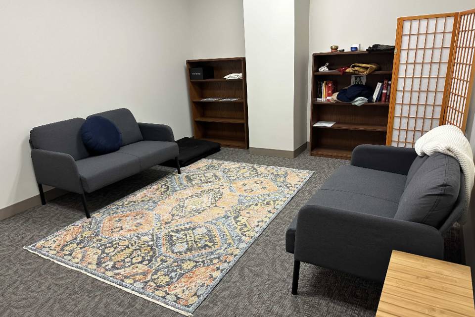 Law School Interfaith A room with sofas along each wall and a rug in the center. There are book shelves in the background with various items visible.