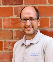 Bobb Wassel Bobby Wassel, headshot, wearing a grey SLU polo shirt, stands in front of a brick wall and smiles.