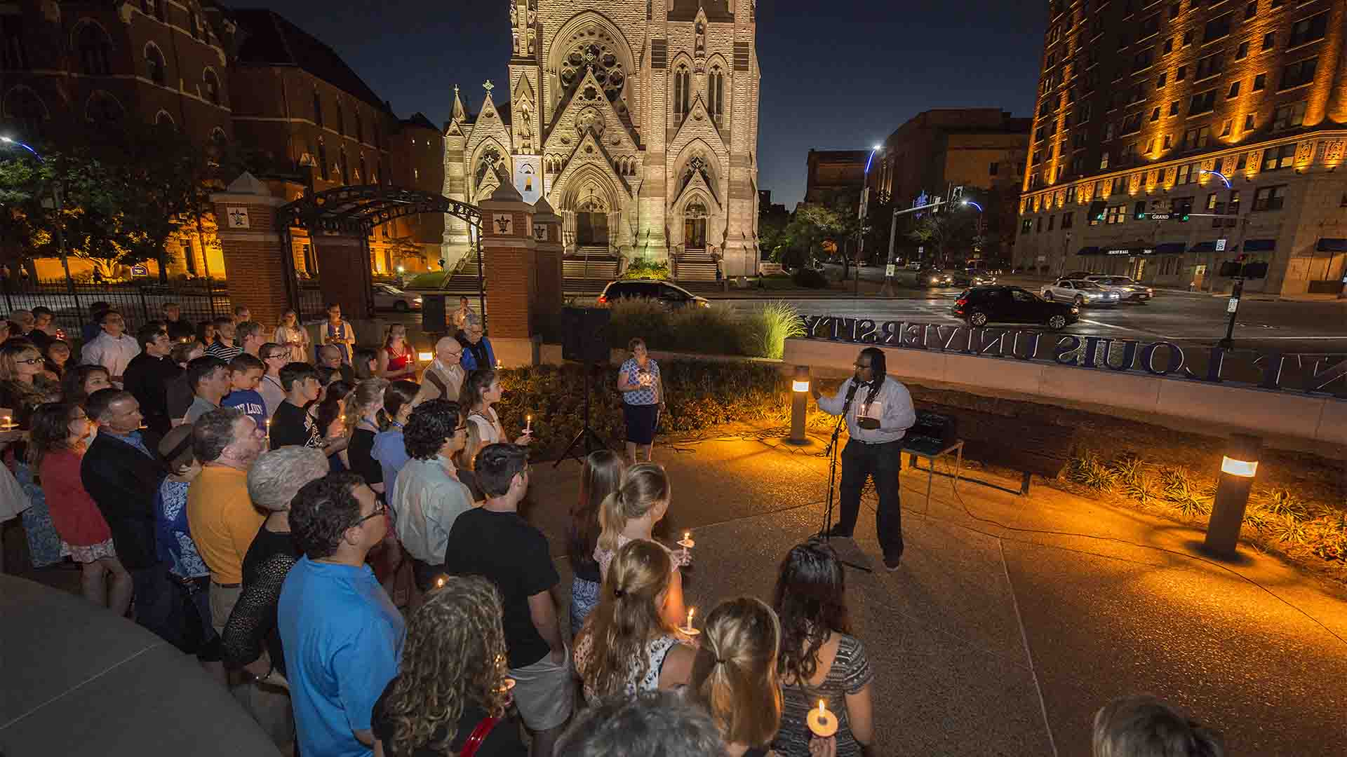 Johnathan Smith Dr. Jonathan Smith stands in front of a group of people at night, at the corner or Lindell and Grand, with the Saint Louis University sign in the background.