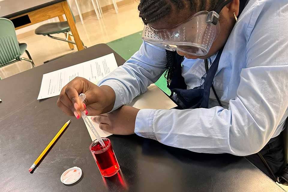 Biome STEAM academy A young girl uses a pipette to get a red liquid out of a beaker.