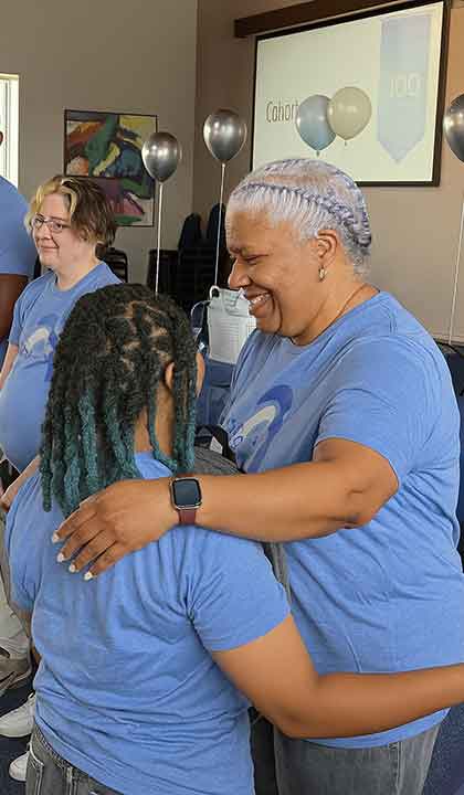 STL Teaching Fellows celebration A woman hugs a younger woman during a celebration. Both are wearing matching STL Teaching Fellows shirts.