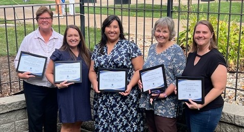 photo of 2024 School of Education faculty and staff award winners Five award winners pose side by side outdoors, holding their certificates.