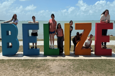 Belize beach SLU students and faculty stand on a 3-D sign with letters that spell out Belize. A beach and ocean are visible in the background.