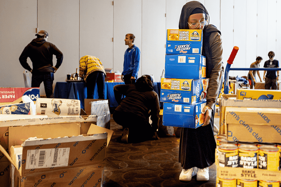 Students stack boxes of food donations inside a large room.