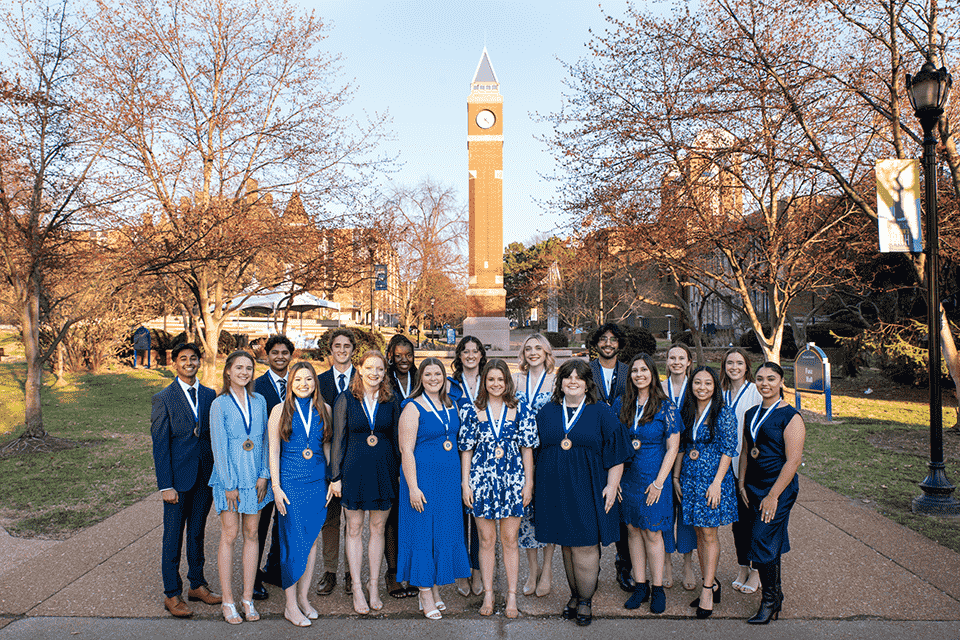 Spriit of the Billiken A group of 18 students wear medals around their neck with the clocktower over their heads in the background.