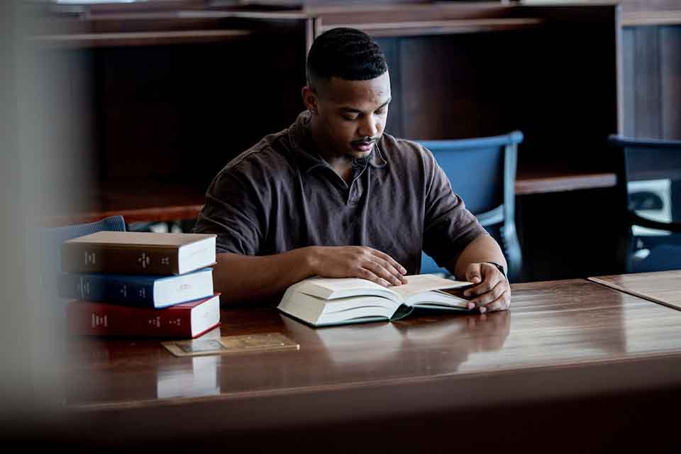 Law student A male student reads from a book at a table in thel library.