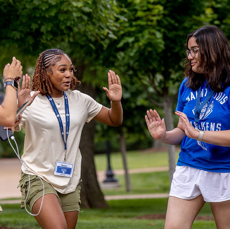 A student raises both hands for high fives while another student looks on.