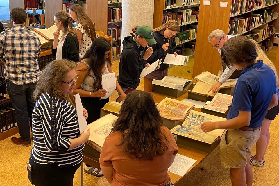 Vatican Film Library Instruction Students and faculty members examine books and other materials around tables and shelves in the library.