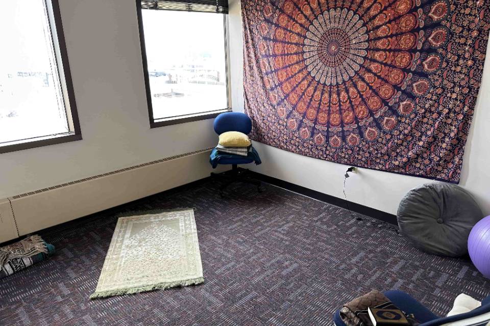 school of nursing space A room has a prayer rug on the floor as well as a mandala tapestry on one wall. Chairs and cushions are also visible.
