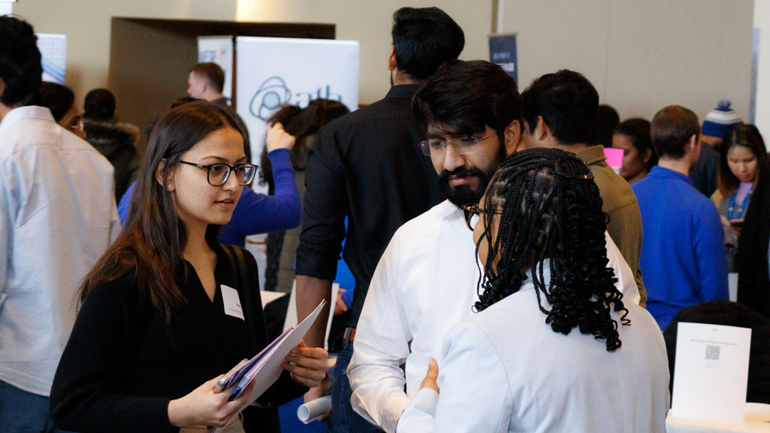 Spring 2025 Career Fair Two students talk to an employer in a room filled with people.