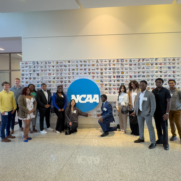 Indy Career Trek 2024 NCAA Students visit the NCAA and are posing in front of a NCAA wall with team logos.