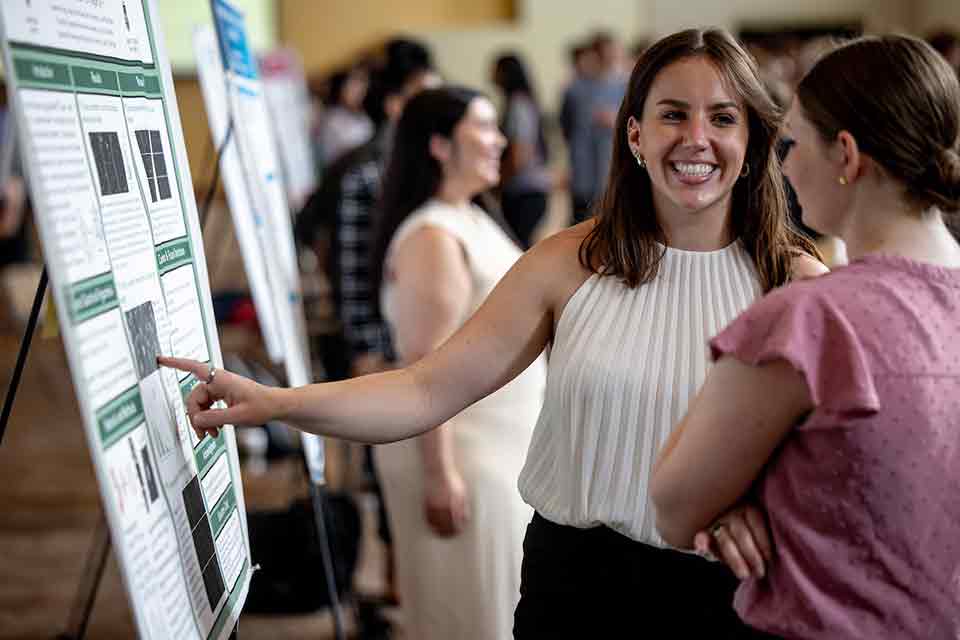 Senior Legacy Symposium A senior smiles as she shows off her research poster to an attendee of the 2024 Senior Legacy Symposium