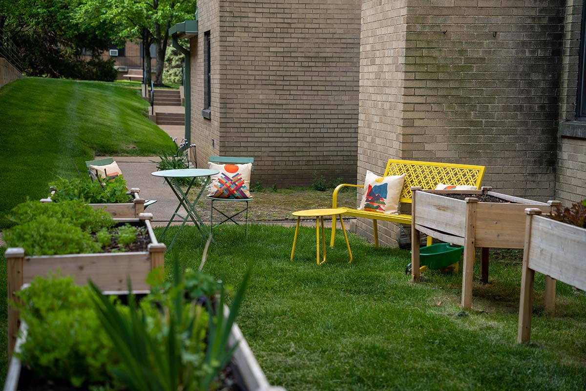 Wuller Gardens WellSPACE Brightly colored chairs sitting on a lawn outside a building with landscape boxes nearby.