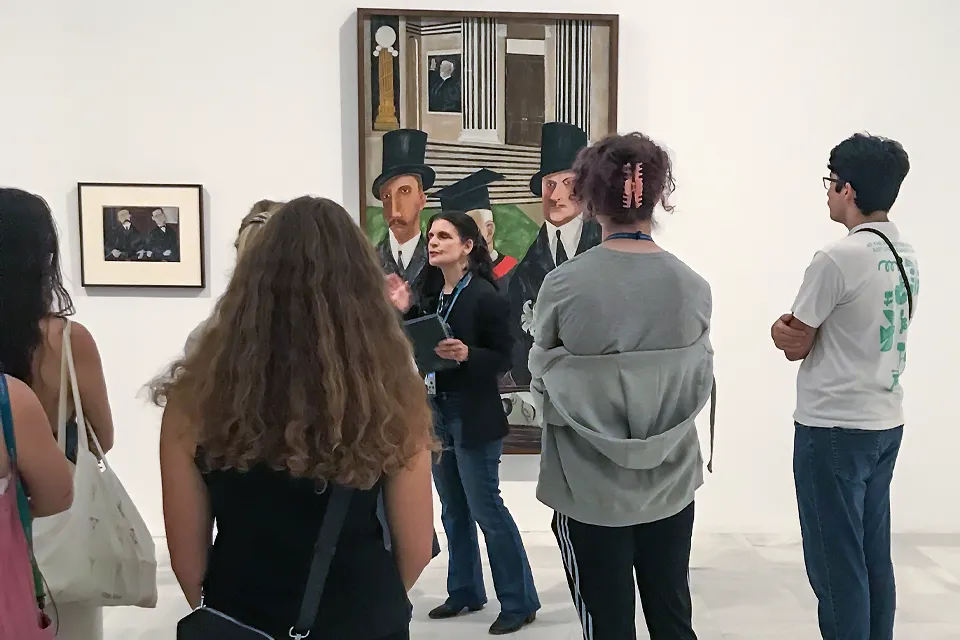Some students attend to a woman talking about some pictures on a wall.