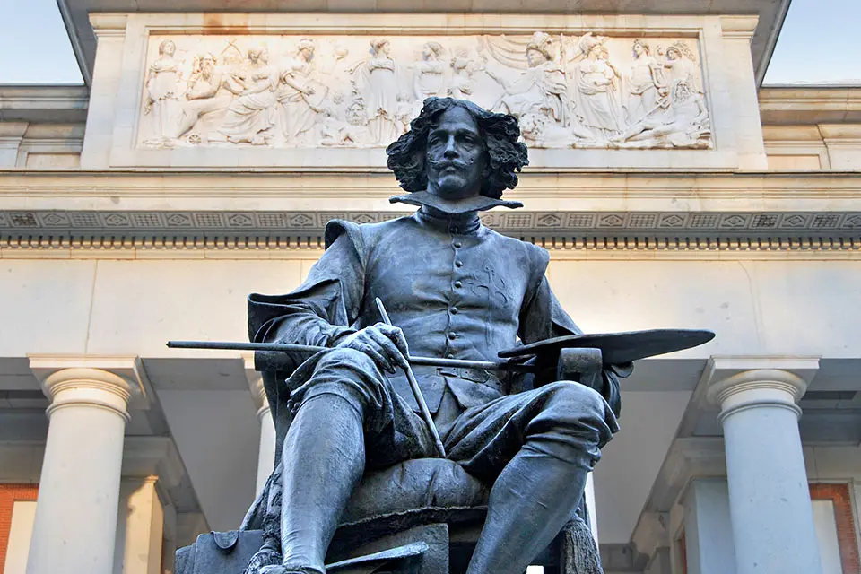 Prado Museum of Madrid Statue of Velazquez in front of the Prado Museum. The figure is seated, holding an artist's palette and paint brushes.