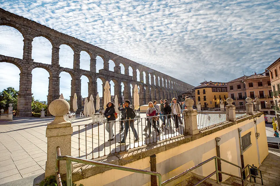 Aqueduct of Segovia A Roman aqueduct with arches made of granite brick stretches itself next to a town.