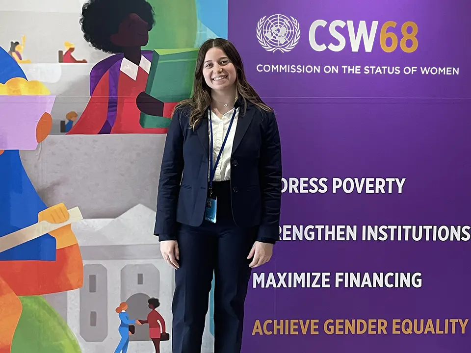Alumna Natalie Alper A student posing in front of of the Commission on the Status of Women poster in the background.