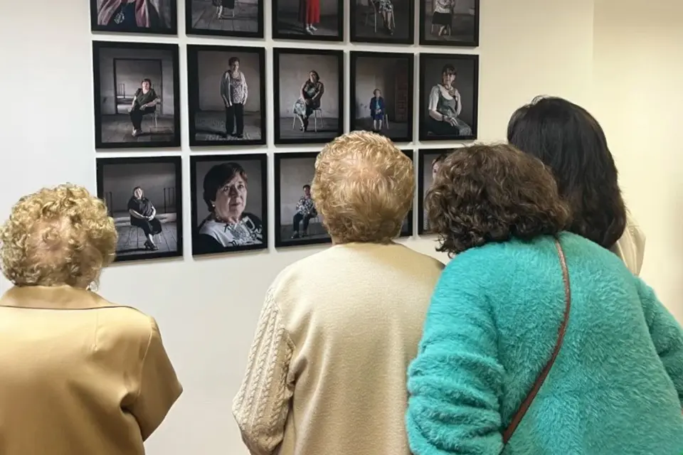 Women photographed in Fischer's "Cardos" work view photos of themselves on display at exhibit. Women look at themselves in photographs hung on wall that are part of an art exhibit.