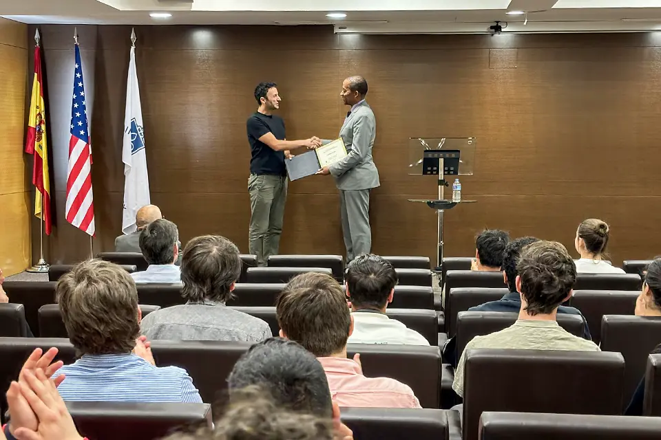 Triplett awarding El Mir with Professorship for Teaching Excellence in the San Ignacio Hall Auditorium on April 25, 2024. A person holding a diploma standing on a stage in front of a group of people hands the diploma to the winner.