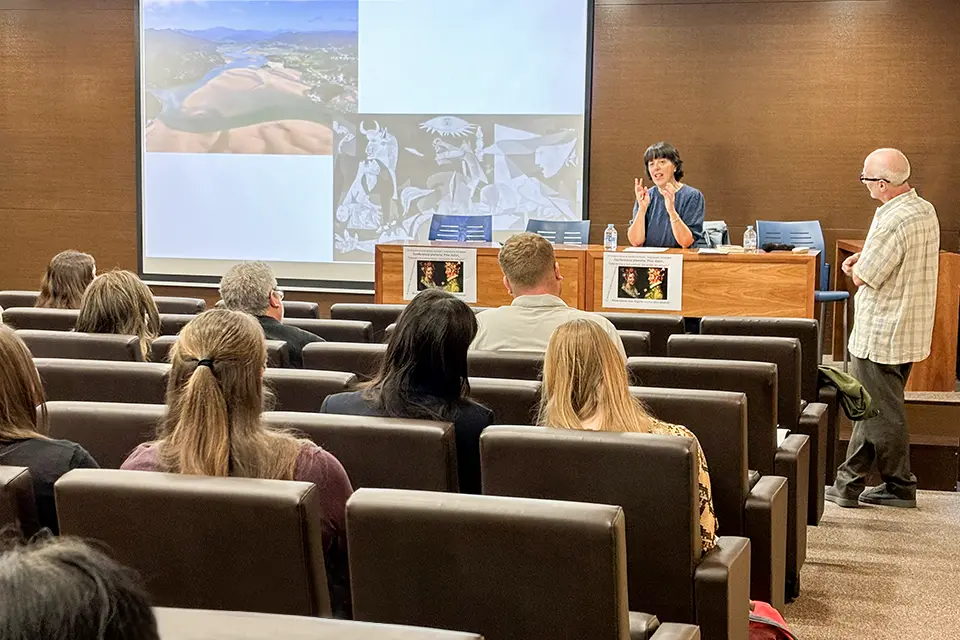 Adón habla durante su ponencia titulada “Literatura y naturaleza: vocación de refugio” en el auditorio de San Ignacio Hall. Una autora sentada presenta su obra a una audiencia de estudiantes y profesores en un auditorio. / An author sitting down presents her work to an audience of students and professors in an auditorium.