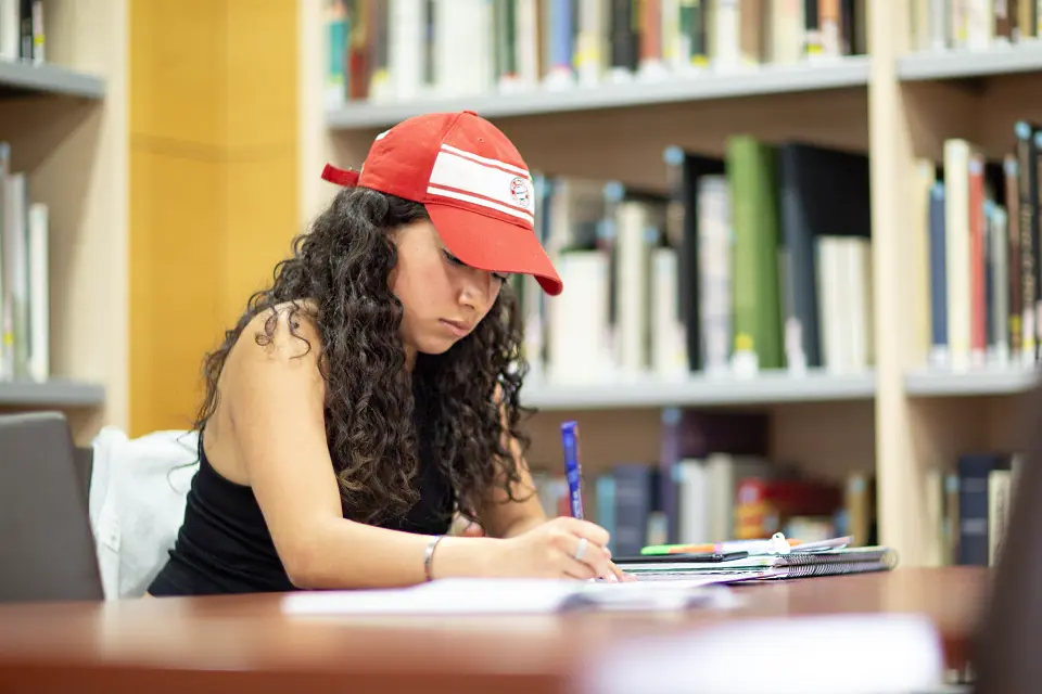 A student in the SLU-Madrid library. A student writing in a notebook in the library