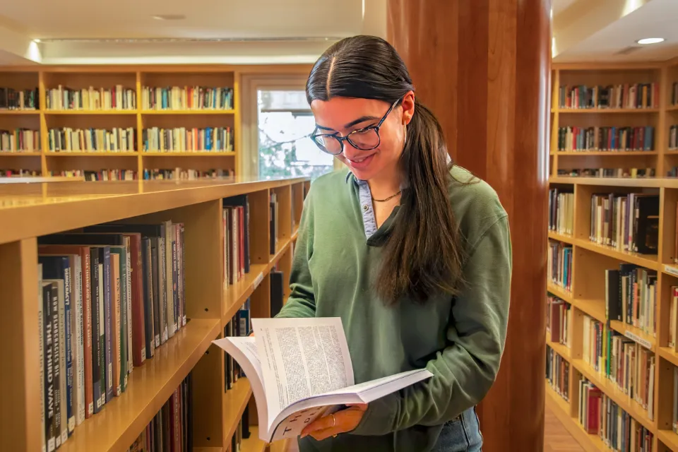 Library Policies A student sitting at a table with a laptop computer while writing in a notebook.