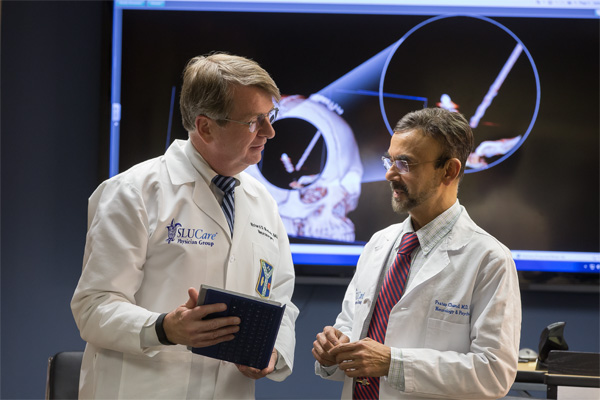 Organizational Two male doctors in white coats chat while reviewing information on a clipboard.