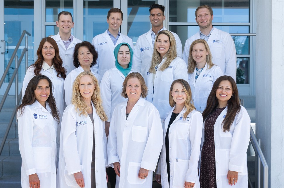 SLU Dermatology Faculty Faculty members wearing white doctors' coats stand in three rows for a group photo.