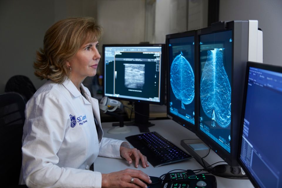 A doctor examines breast imaging scans on a computer screen.