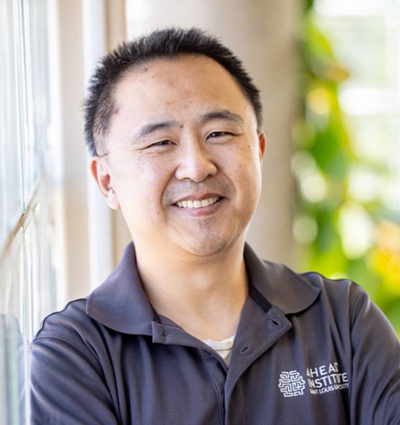 Zidong Zhang, Ph.D., research scientist of the AHEAD Institute at Saint Louis University School of Medicine. A man poses for a photo indoors next to a window. He smiles for the camera.