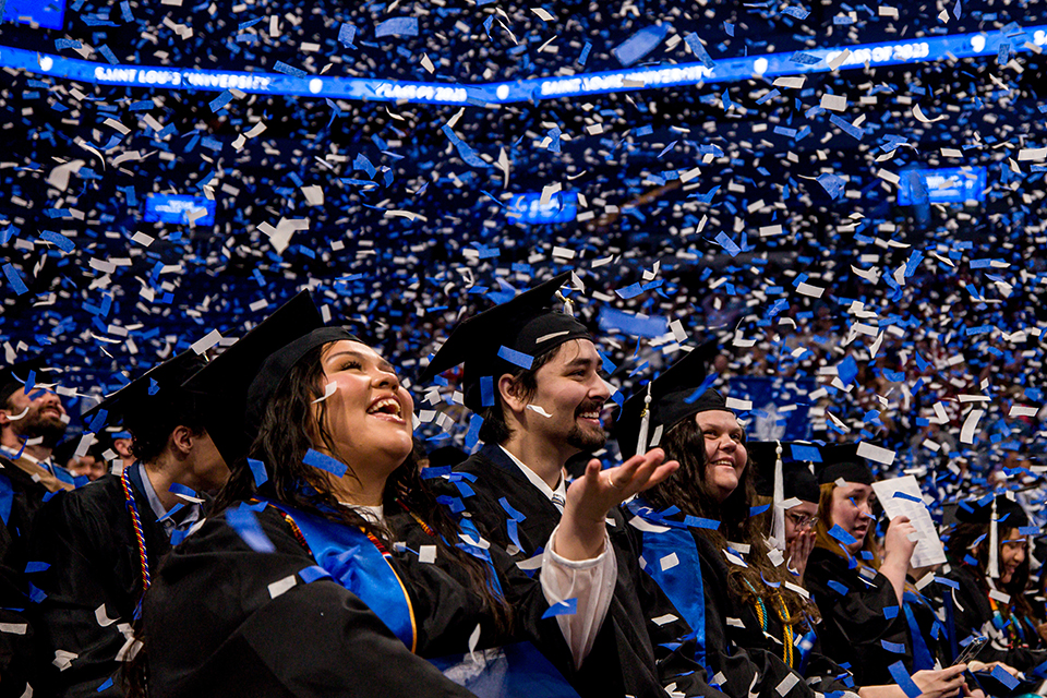 SLU Commencement Graduates sit in chairs in the bowl of Chaifetz Arena. Confetti falls around them.