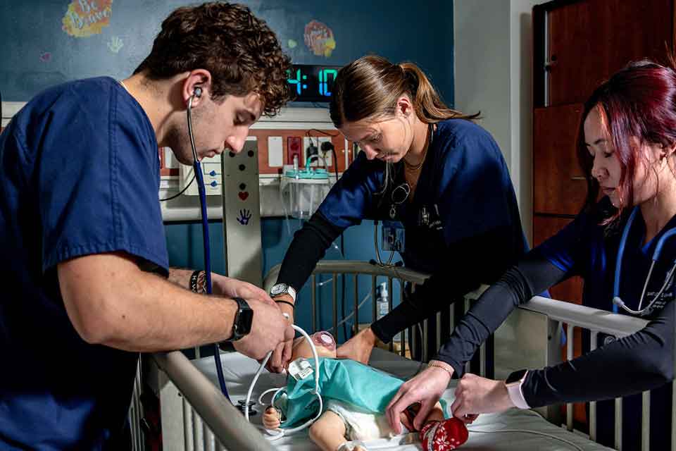 Nursing Degree Programs Three nursing students treat a simulated infant patient in a SLU nursing lab.