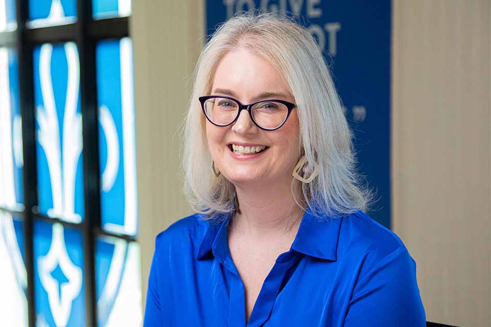 Tina A woman in glasses and a blue shirt stands in front of a glass wall with an inverted SLU logo