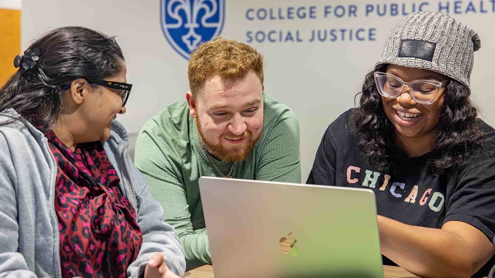 Three students gather around a laptop and laugh while talking.