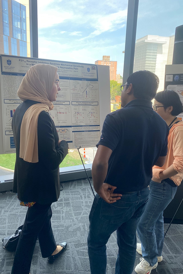 SLU student presents research during the forum poster session. Two attendees hold a discussion in front of a research poster.
