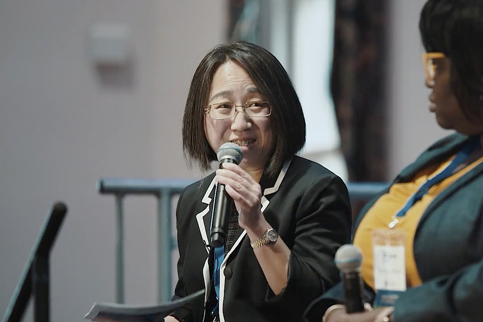Tang speaking at the Be Heard: Women in Leadership Conference. A woman sits and smiles while holding a microphone.